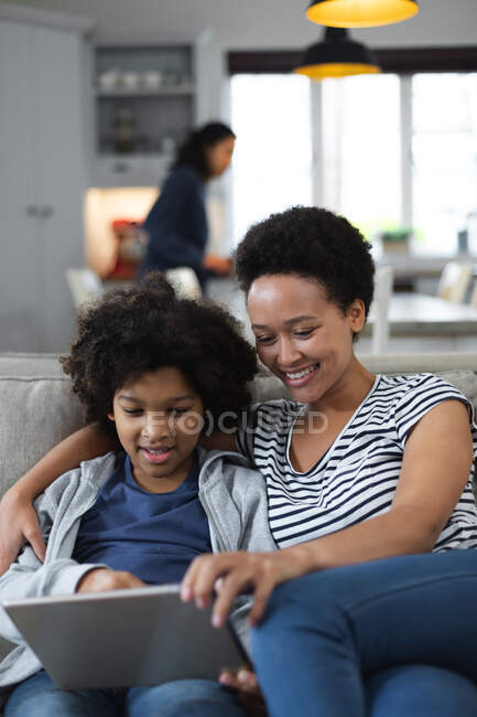 Femme et fille de race mixte assis sur le canapé à l'aide d'une tablette numérique. auto isolement qualité famille temps à la maison ensemble pendant coronavirus covid 19 pandémie. — Photo de stock