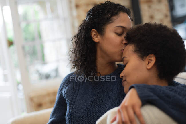 Mixed race lesbian couple kissing on forehead in kitchen. self isolation quality time at home together during coronavirus covid 19 pandemic. — Stock Photo