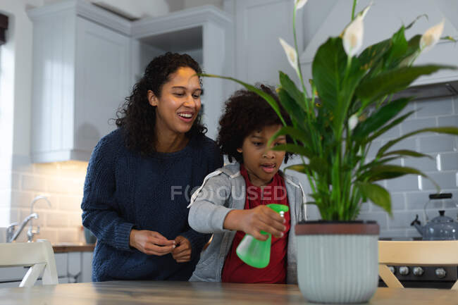 Mixte femme race et fille arrosage plantes dans la cuisine. auto isolement qualité famille temps à la maison ensemble pendant coronavirus covid 19 pandémie. — Photo de stock