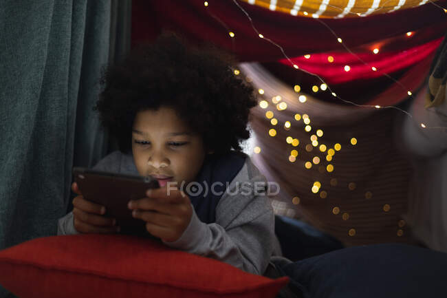 Mixed race girl lying in couch fort using digital tablet. self isolation quality family time at home together during coronavirus covid 19 pandemic. — Stock Photo