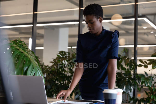 Mixed race businesswoman standing using laptop going through paperwork in modern office. business modern office workplace technology. — Stock Photo