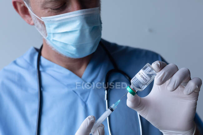 Médico do sexo masculino, caucasiano, com máscara facial em pé e seringa de enchimento. profissional médico de saúde higiene do trabalhador durante coronavírus covid 19 pandemia. — Fotografia de Stock