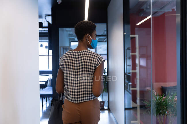 Gemischte Rasse Geschäftsfrau mit Gesichtsmaske geht in modernen Büros. Business moderne Büroarbeitstechnologie. — Stockfoto