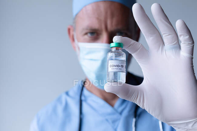 Caucasian male doctor wearing face mask standing and showing coronavirus vaccine. medical professional healthcare worker hygiene during coronavirus covid 19 pandemic. — Stock Photo