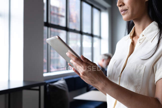Змішана гоночна бізнес-леді стоїть за допомогою цифрового планшета в сучасному офісі. бізнес сучасні технології офісного робочого місця . — стокове фото