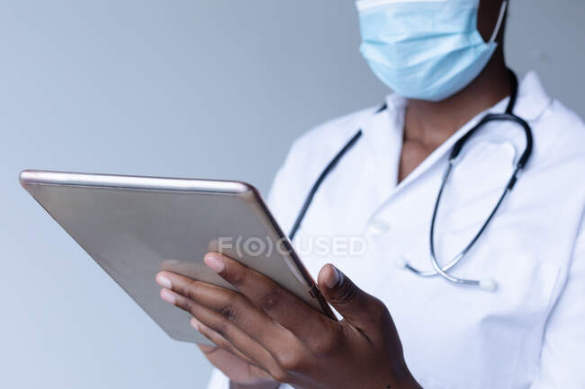 Médecin de race mixte portant un masque facial debout et utilisant une tablette numérique. professionnel de la santé hygiène du personnel de santé pendant le coronavirus covid 19 pandémie. — Photo de stock
