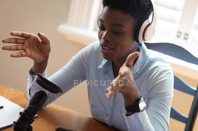 Femme afro-américaine portant des écouteurs utilisant un microphone et un ordinateur portable. communication en ligne, rester à la maison en isolement pendant le confinement en quarantaine. — Photo de stock