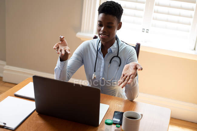 Médico afroamericano haciendo videollamada usando laptop. telemedicina durante el autoaislamiento en cuarentena. - foto de stock