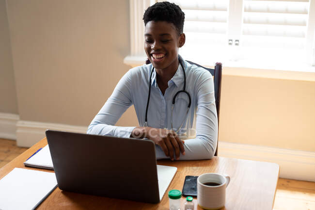 Médico afroamericano haciendo videollamada usando laptop. telemedicina durante el autoaislamiento en cuarentena. - foto de stock
