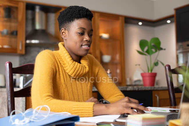 Африканская американка носит ноутбук и улыбается на кухне. оставаться .