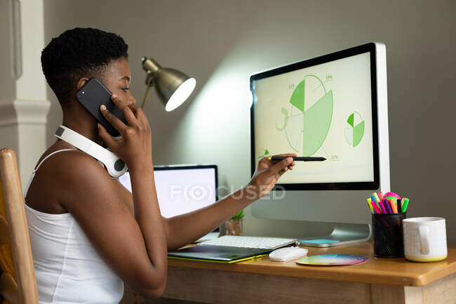 Африканская американка разговаривает на смартфоне и пользуется компьютером, работая из дома. оставаться дома в изоляции в карантинной изоляции — стоковое фото