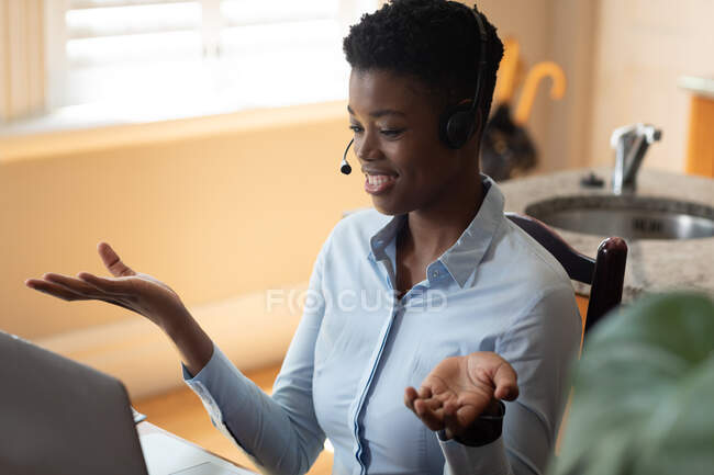 African american woman wearing phone headset making a video call in kitchen. staying at home in self isolation during quarantine lockdown. — Stock Photo
