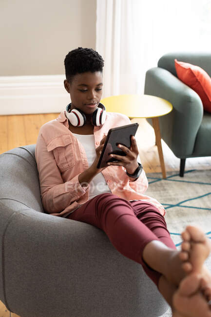Mulher afro-americana sentada em hassock usando tablet digital trabalhando em casa. ficar em casa em auto-isolamento durante o confinamento de quarentena. — Fotografia de Stock