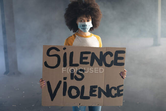 Mulher de raça mista usando máscara facial com slogan segurando sinal de protesto. gênero fluido lgbt identidade conceito de igualdade racial. — Fotografia de Stock