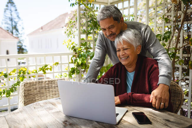 Senior couple afro-américain assis sur la terrasse à l'aide d'un ordinateur portable. mode de vie à la retraite en isolement personnel pendant une pandémie de coronavirus covid 19. — Photo de stock