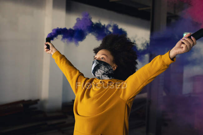 Femme de race mixte portant un masque facial tenant une fusée éclairante bleue. genre fluide identité lgbt concept d'égalité raciale. — Photo de stock