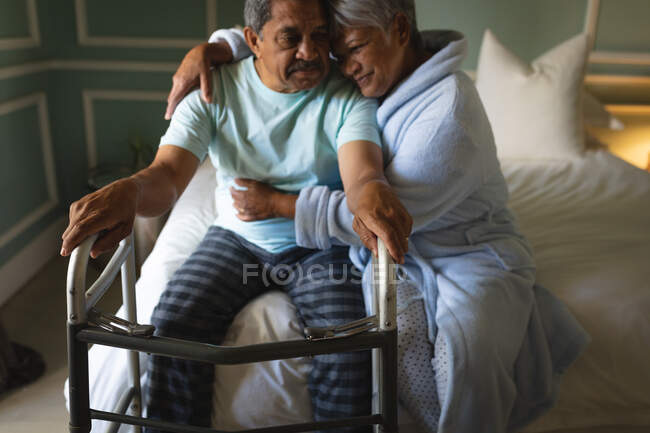 Старшая африканская американская пара, сидящая на кровати, обнимаясь в спальной комнате. Пенсионный образ жизни в самоизоляции во время пандемии коронавируса. — стоковое фото