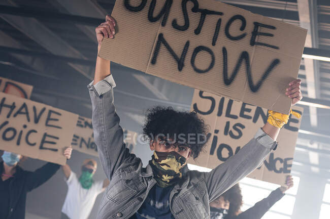 Grupo multiétnico de personas que usan máscaras faciales con carteles de protesta. género fluido lgbt identidad concepto de igualdad racial. - foto de stock