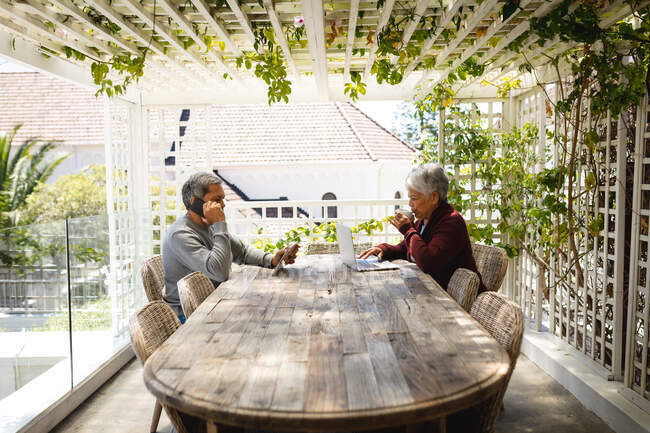 Старша афроамериканська пара сидить на терасі, використовуючи ноутбук і цифровий планшет. Життя на пенсії в самоізоляції під час коронавірусної ковини 19 пандемії. — стокове фото