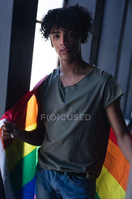 Mixed race man holding rainbow flag looking at camera. gender fluid lgbt identity racial equality concept. — Stock Photo