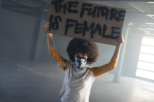 Gemischte Frau mit Gesichtsmaske und Protestschild. Geschlecht fluid lgbt Identität rassische Gleichberechtigung Konzept. — Stockfoto