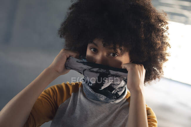 Mujer de raza mixta poniendo una mascarilla en mirar a la cámara. género fluido lgbt identidad concepto de igualdad racial. - foto de stock