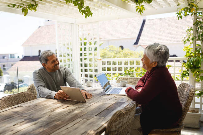 Senior african american couple sitting on terrace using laptop and digital tablet. retirement lifestyle in self isolation during coronavirus covid 19 pandemic. — Stock Photo