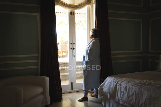 Femme afro-américaine âgée debout près d'une fenêtre dans une chambre à coucher. mode de vie à la retraite en isolement personnel pendant une pandémie de coronavirus covid 19. — Photo de stock