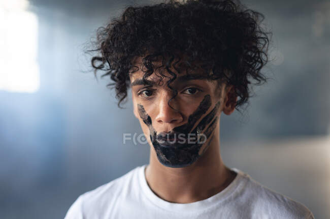 Человек смешанной расы с черным отпечатком руки, нарисованным на лице, смотрящим в камеру. Концепция гендерного расового равенства. — стоковое фото