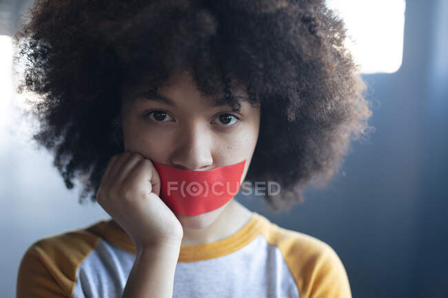 Donna di razza mista con nastro adesivo sulla bocca guardando la fotocamera. genere fluido lgbt identità concetto di uguaglianza razziale. — Foto stock