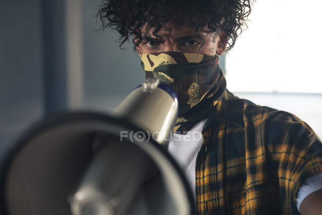 Homme de race mixte portant un masque facial criant en mégaphone. genre fluide identité lgbt concept d'égalité raciale. — Photo de stock