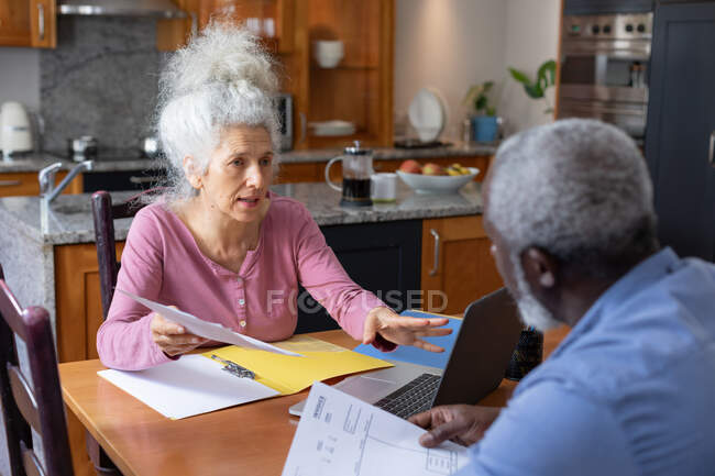 Senior mixed race couple using laptop paying bills together in dining room. staying at home in self isolation during quarantine lockdown. — Stock Photo