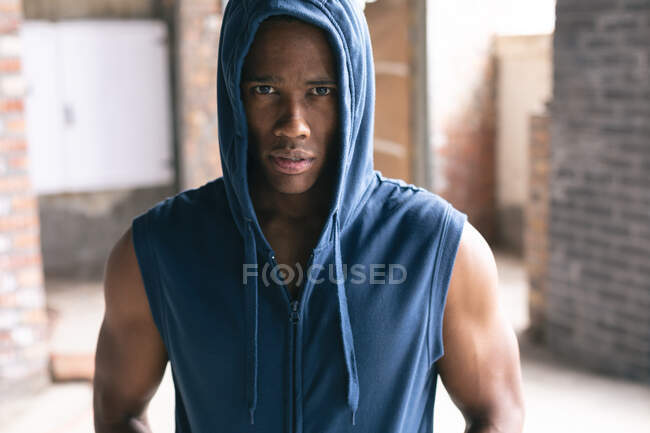 Ritratto di uomo afroamericano che indossa una felpa con cappuccio e guarda la telecamera in un edificio urbano vuoto. fitness urbano stile di vita sano. — Foto stock