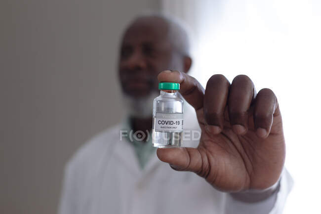 Старший африканский врач-американец держит ковид 19 вакцин у себя дома. медицинское обслуживание в домашних условиях в изоляции во время карантинной изоляции. — стоковое фото