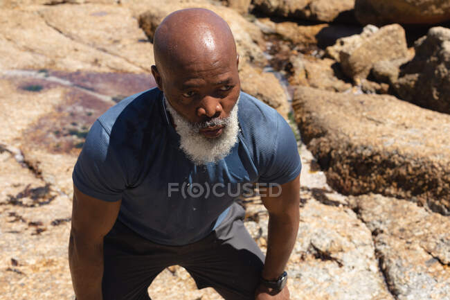 Un homme afro-américain expérimenté qui fait de l'exercice au soleil reprenant son souffle. retraite saine sport forme physique extérieure mode de vie. — Photo de stock