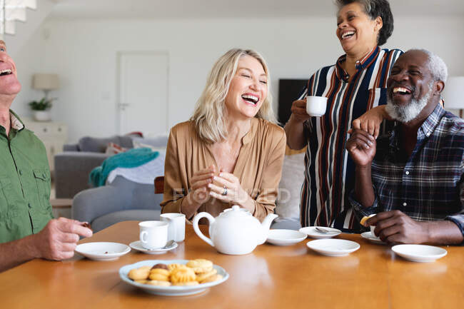 Ältere kaukasische und afrikanisch-amerikanische Paare sitzen zu Hause am Tisch und trinken Tee. Senioren-Lebensstil Freunde Geselligkeit. — Stockfoto
