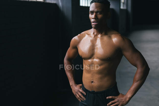 Uomo afroamericano in piedi e flettendo i muscoli in un edificio urbano vuoto. fitness urbano stile di vita sano. — Foto stock