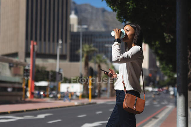 Afroamerikanerin mit Smartphone beim Kaffeetrinken auf der Straße. Lebensstil-Konzept während Coronavirus-Covid 19 Pandemie. — Stockfoto