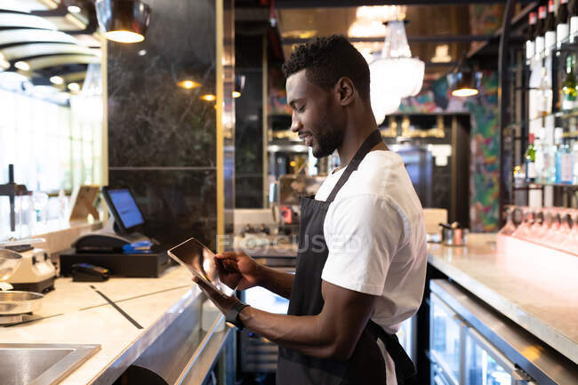 African american male barista standing behind a bar using a digital tablet and smiling. independent small business owner. — Stock Photo