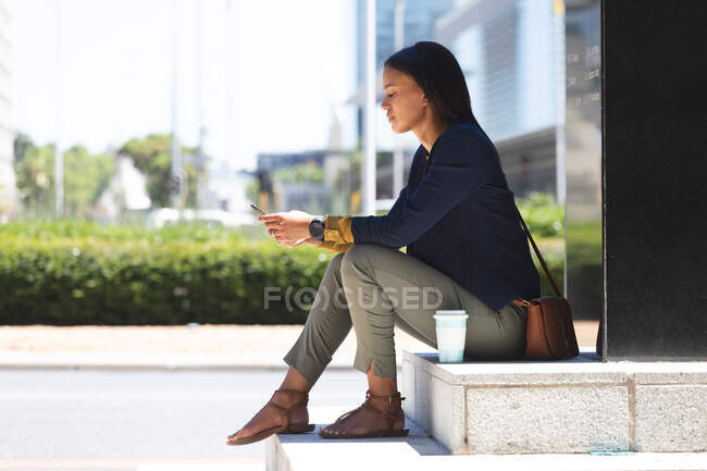 African american woman using smartphone while sitting at corporate park. lifestyle living during coronavirus covid 19 pandemic. — Stock Photo