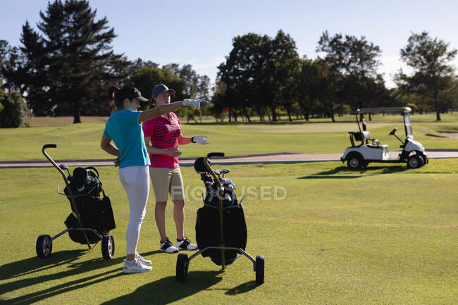 Две белые женщины с сумками для гольфа разговаривают на поле для гольфа. спорт досуг хобби гольф здоровый образ жизни на открытом воздухе. — стоковое фото