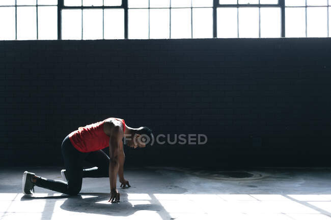 Afrikanischer Mann in Sportkleidung kniet in leerem städtischen Gebäude und beginnt zu rennen. urbane Fitness gesunder Lebensstil. — Stockfoto