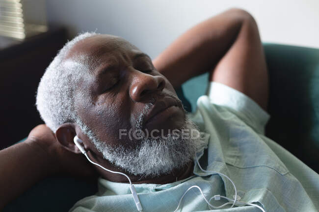 Uomo anziano afroamericano sdraiato sul divano che dorme ascoltando musica sugli auricolari. stare a casa in isolamento durante l'isolamento in quarantena. — Foto stock