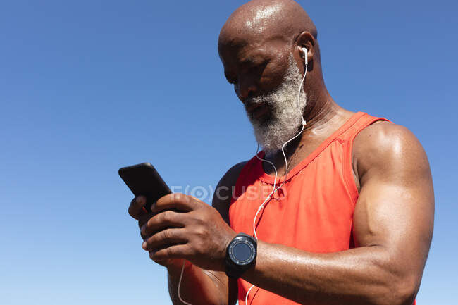 Fit Senior-Afroamerikaner trägt Kopfhörer mit Smartphone in der Sonne. gesunde Ruhestand Technologie Kommunikation Outdoor Fitness Lebensstil. — Stockfoto