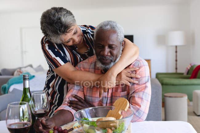 Coppia di anziani afroamericani seduti a tavola a cenare e ad abbracciarsi a casa. anziani amici di stile di vita di pensione socializzare. — Foto stock