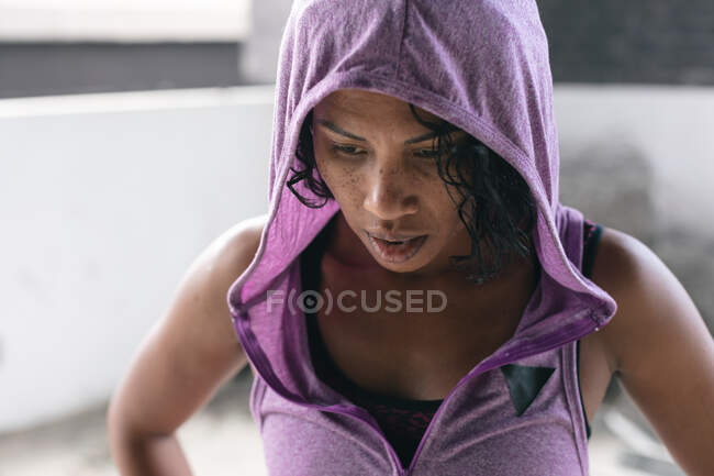 Retrato de una mujer afroamericana con capucha en un edificio urbano vacío. aptitud urbana estilo de vida saludable. - foto de stock