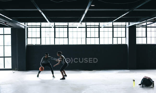 Hombre y mujer afroamericanos de pie en un edificio urbano vacío y jugando baloncesto. aptitud urbana estilo de vida saludable. - foto de stock