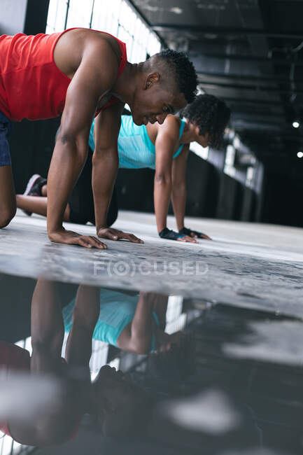African american man and woman wearing sports clothes doing push ups in empty urban building. urban fitness healthy lifestyle. — Stock Photo