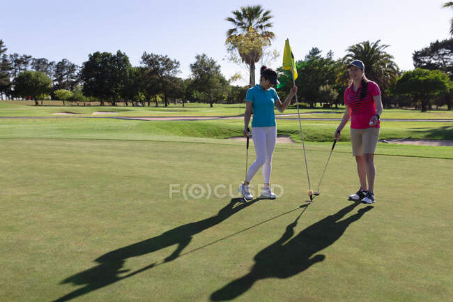 Zwei kaukasische Frauen spielen Golf, eine holt die Fahne aus dem Loch. Sport Freizeit Hobbys Golf gesunder Lebensstil im Freien. — Stockfoto