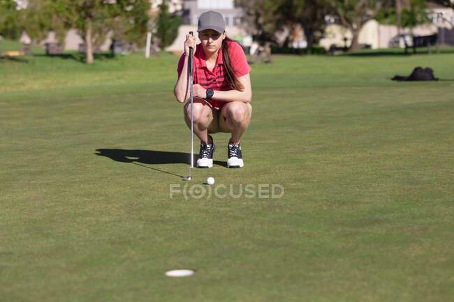 Белая женщина играет в гольф на корточках перед тем, как выстрелить в лунку. спорт досуг хобби гольф здоровый образ жизни на открытом воздухе. — стоковое фото